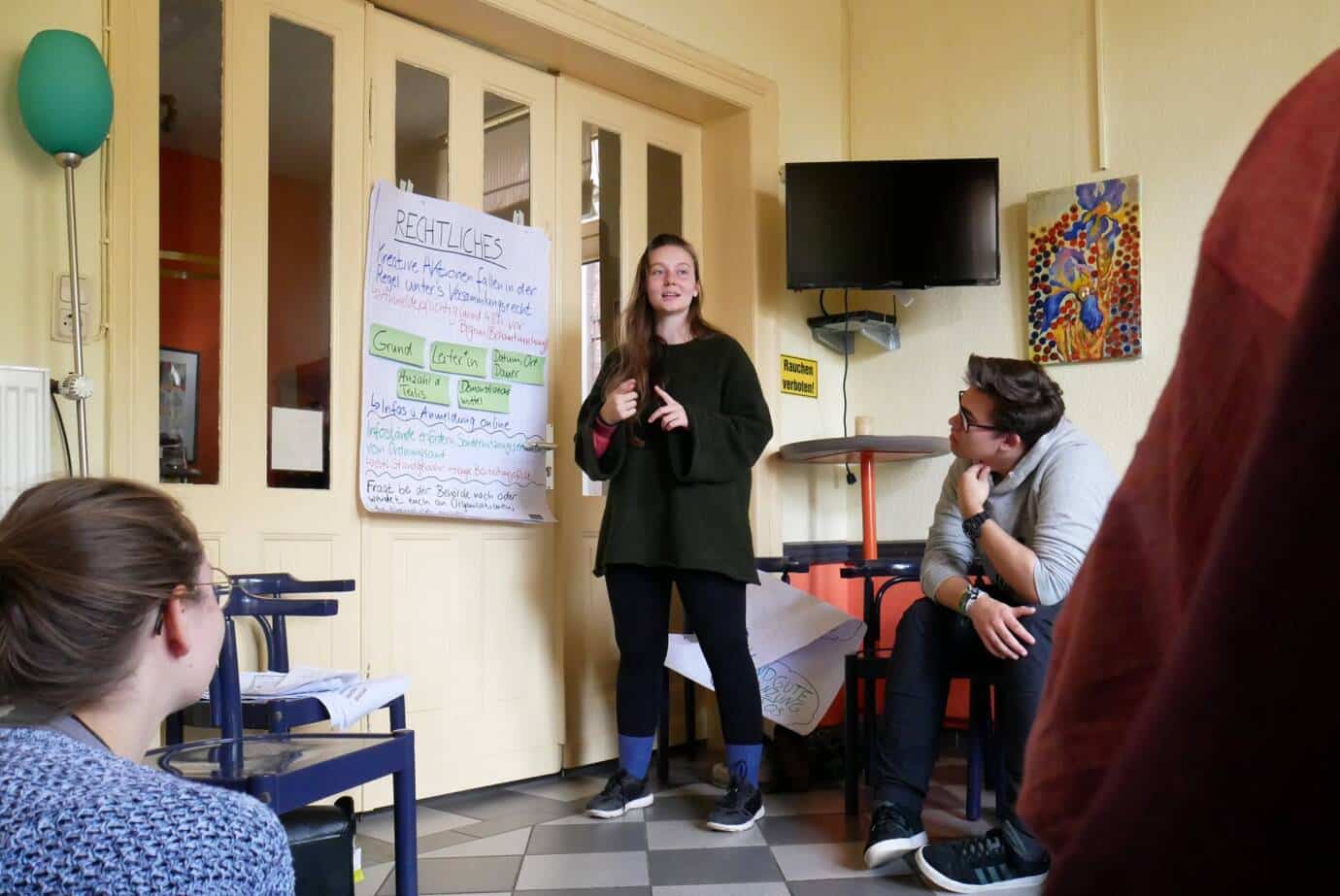 Person hält Präsentation vor Gruppe in Zimmer.