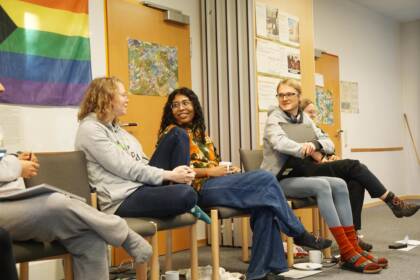 Gruppe diskutiert vor Regenbogenflagge im Raum.