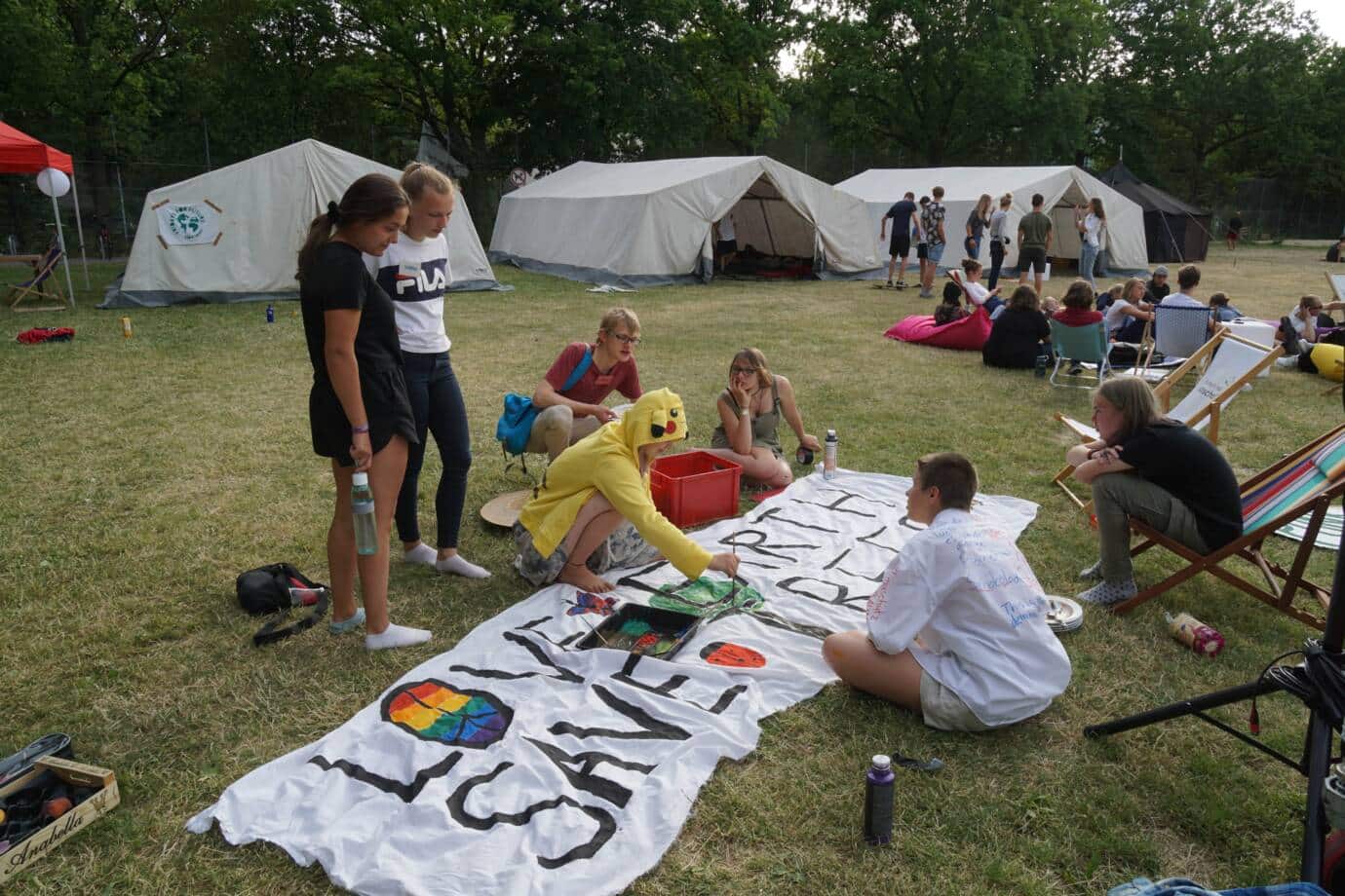 Jugendliche bemalen Banner vor Zelten