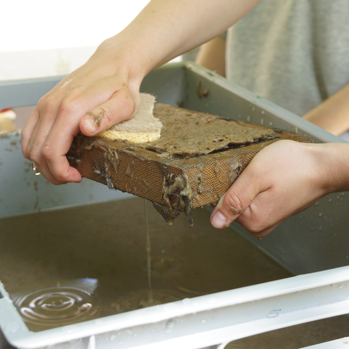 Handwerkliche Papierherstellung mit Holzrahmen und Wasserbecken.