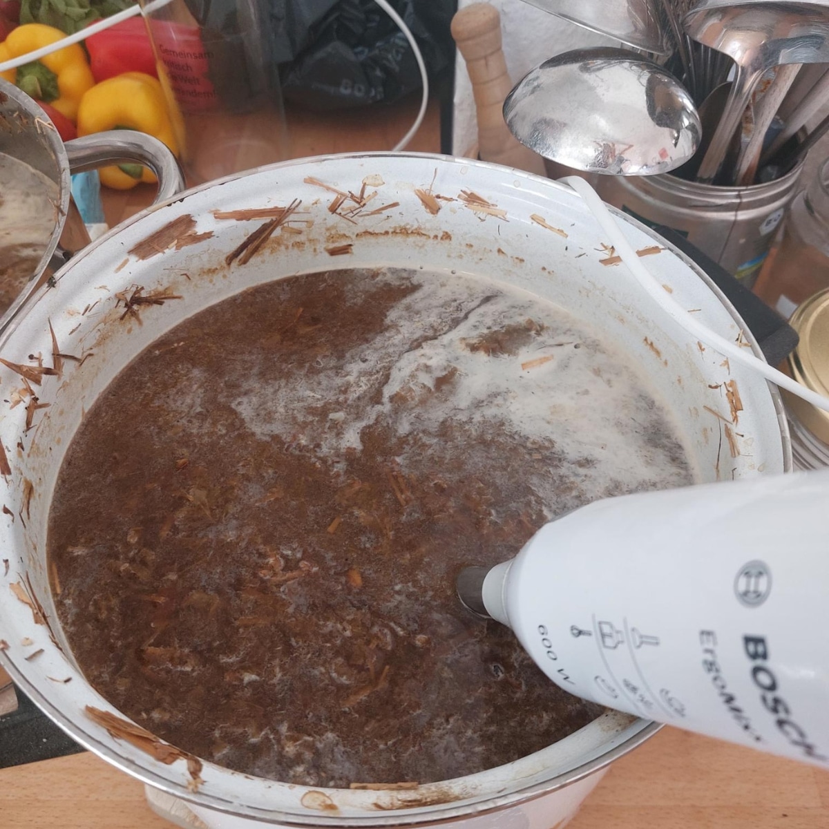 Suppentopf mit Pürierstab, Zutaten im Hintergrund.