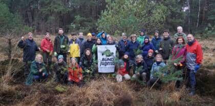 Gruppe pflanzt Bäume im Wald, hält Banner.